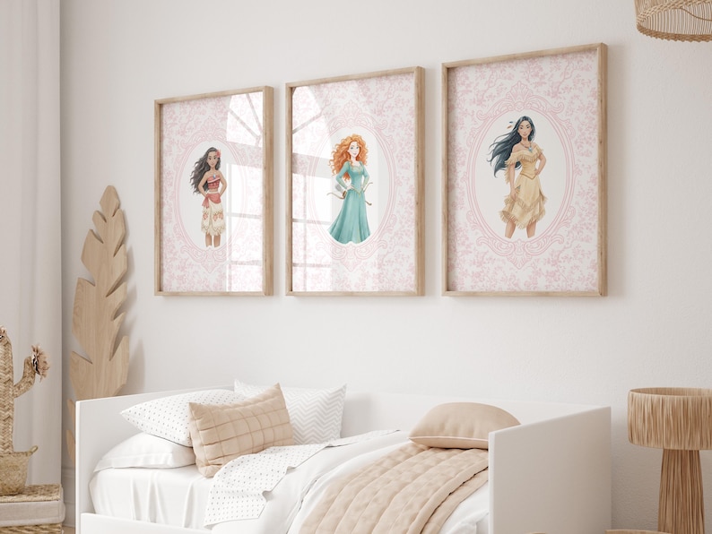 May include: Three framed art prints featuring illustrations of animated characters. Each print has a light wood frame and a pink damask background. The characters are in oval frames. The prints are hung above a white bed.