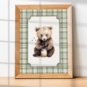 May include: A framed watercolor print featuring a brown bear cub holding a jar of honey. The artwork is set against a white background with a green plaid border and a natural wood frame. The image has a whimsical, childlike quality.
