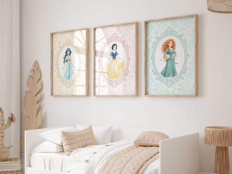 May include: Three framed art prints featuring watercolor illustrations of princesses. Each princess is depicted within an oval frame against a patterned background. The frames are displayed above a white bed with neutral-toned bedding.