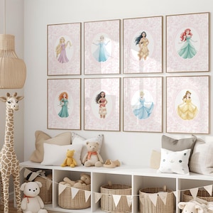 May include: A collection of eight framed art prints featuring watercolor illustrations of fairytale princesses. Each print has a pink floral background and a gold frame. The princesses are depicted in their iconic gowns and poses.