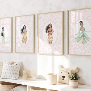 May include: Four framed art prints featuring watercolor illustrations of animated characters. Each print has a light wood frame and a pink floral background. The characters are in oval frames. Decorative pillows and a bear-shaped pillow are on a white shelf.