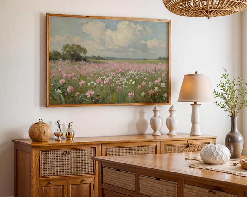 Peut inclure: Une peinture encadr&eacute;e repr&eacute;sente un paysage avec un champ de fleurs roses et blanches sous un ciel nuageux. Le tableau est accroch&eacute; au-dessus d'un buffet en bois avec des panneaux tress&eacute;s. Une lampe avec un abat-jour beige et des vases d&eacute;coratifs sont sur le buffet.