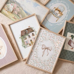 Peut inclure: Plusieurs tirages d'art encadr&eacute;s avec des illustrations &agrave; l'aquarelle. Les impressions pr&eacute;sentent une maison, un chien sur une chaise, un n&oelig;ud, un canard et un paysage avec un arbre. Les cadres sont en bois clair.