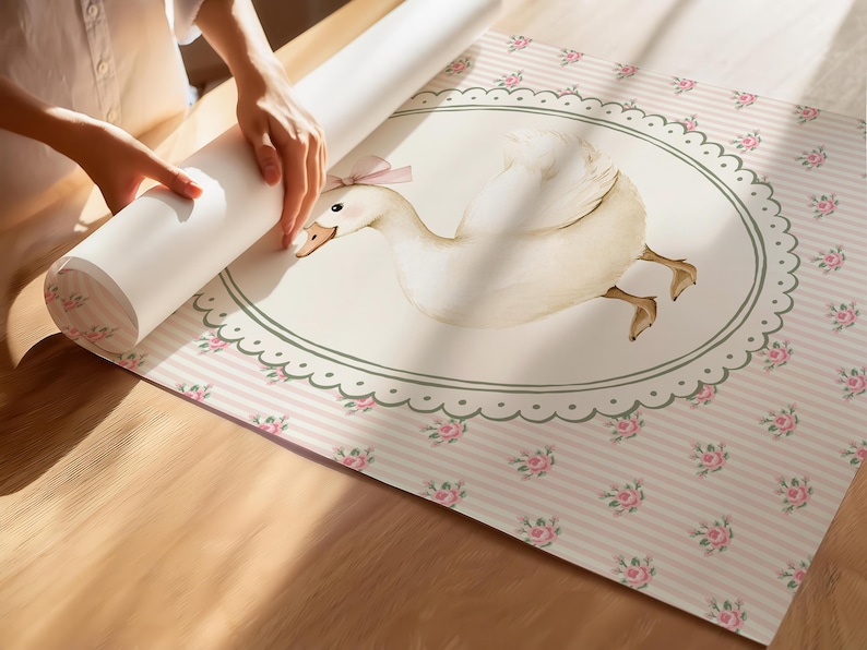 Peut inclure: Un rouleau de papier peint en cours de d&eacute;roulement, r&eacute;v&eacute;lant un motif fantaisiste. Le papier peint pr&eacute;sente une grande illustration d'une oie blanche avec un n&oelig;ud rose, dans un cadre ovale. Le fond est &agrave; rayures roses et &agrave; petits motifs de roses.