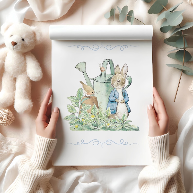 Puede incluir: Ilustraci&oacute;n en acuarela de Peter Rabbit con una chaqueta azul, de pie cerca de una regadera y un p&aacute;jaro. La obra de arte est&aacute; en un bloc blanco con remolinos decorativos azules. Un oso de peluche blanco y hojas de eucalipto est&aacute;n en el fondo.