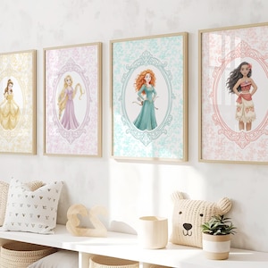 May include: Four framed art prints featuring Disney princesses: Belle in a yellow gown, Rapunzel in a purple dress, Merida in a teal dress, and Moana in a red top and floral skirt. Each princess is set against a patterned background within an oval frame.