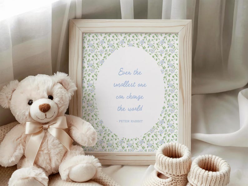 Puede incluir: Un cuadro enmarcado con la cita "Incluso el m&aacute;s peque&ntilde;o puede cambiar el mundo" de Peter Rabbit. Un oso de peluche blanco con una cinta crema y un par de botines de beb&eacute; est&aacute;n junto al marco. La impresi&oacute;n tiene un dise&ntilde;o floral.