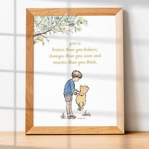 May include: A framed print featuring a watercolor illustration of a boy and a bear. The boy, in a blue shirt and shorts, holds the bear. The print includes the text: "You're braver than you believe, stronger than you seem and smarter than you think."