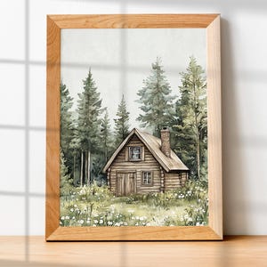 May include: Watercolor painting of a rustic cabin nestled in a forest of tall green trees. The cabin is brown with a chimney and small windows. White wildflowers dot the grassy foreground. The artwork is framed in a light brown wooden frame.