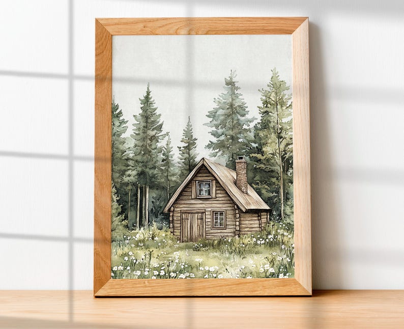 May include: Watercolor painting of a rustic cabin nestled in a forest of tall green trees. The cabin is brown with a chimney and small windows. White wildflowers dot the grassy foreground. The artwork is framed in a light brown wooden frame.