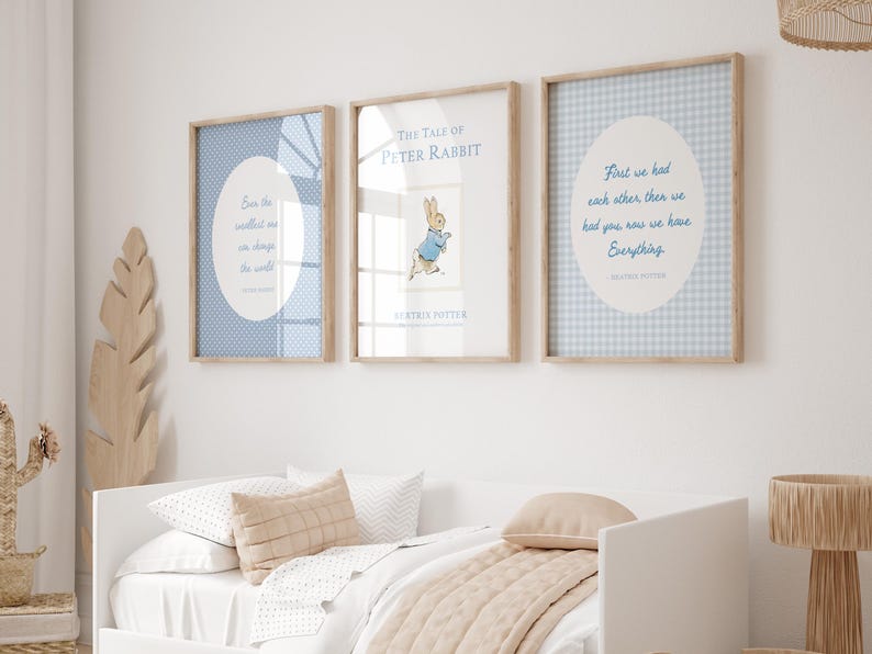 Puede incluir: Tres impresiones enmarcadas con marcos de madera clara cuelgan sobre una cama blanca. Las impresiones presentan patrones y citas en azul y blanco. La impresi&oacute;n central es una portada del libro "The Tale of Peter Rabbit".
