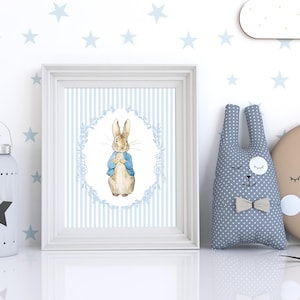Puede incluir: Una impresi&oacute;n enmarcada con una ilustraci&oacute;n en acuarela de un conejo con una chaqueta azul, sobre un fondo a rayas azules y blancas. Junto a ella, un peluche de conejo gris con pajarita, una luna creciente y una linterna en forma de estrella.
