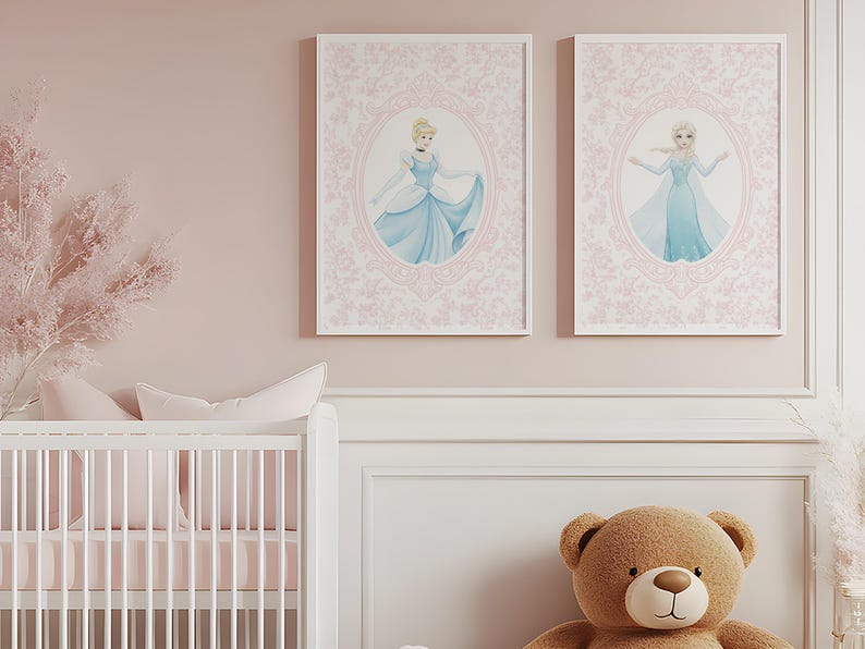 May include: Two framed prints featuring illustrations of princesses in blue gowns, set against a pink floral background. The prints are displayed above a white crib and a large teddy bear, creating a soft, feminine nursery theme.