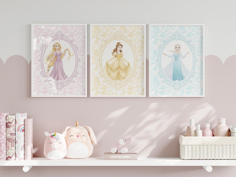 May include: Three framed princess art prints. Each features a different princess in an oval frame with a floral background. The prints are in pastel colors and are displayed above a shelf with toys and books.