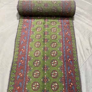 May include: A green, blue, and red patterned runner rug with a fringe border. The rug has a traditional design with repeating geometric shapes.