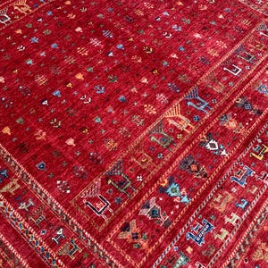 May include: A vibrant red rug with an intricate pattern. The rug features a central field of red with small, scattered motifs in various colors. Borders are adorned with geometric and animal figures in shades of blue, green, and orange. The rug's design is symmetrical and detailed.
