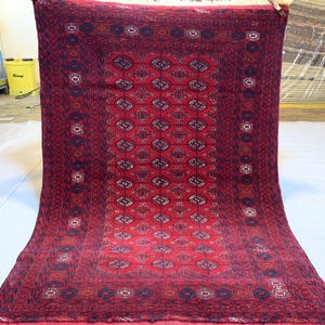 May include: A red rug with a geometric pattern in black and white. The rug has a border with a repeating design.