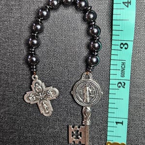 May include: Black beaded rosary bracelet with a silver St. Benedict medal and a silver cross with five small figures. The bracelet is about 2 inches long.
