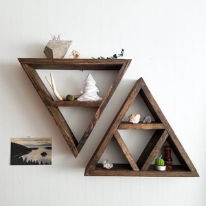 May include: Two triangular wooden shelves with multiple shelves. The top shelf has a small concrete geometric object, a small white tree, and a small antler. The bottom shelf has a small cactus, a small candle, and a small bottle.