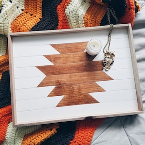 May include: A white wooden tray with a geometric design in brown wood. The tray has a small candle and an owl pendant on it.