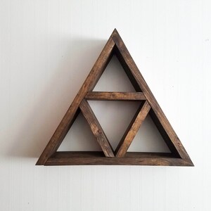 May include: A dark brown wooden triangle shelf with three shelves. The shelf is mounted on a white wall.