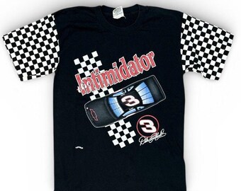 May include: Black t-shirt featuring a race car design with the word "Intimidator" in red. The shirt has checkered sleeves and a graphic of a race car with the number "3". The design includes the signature of Dale Earnhardt.