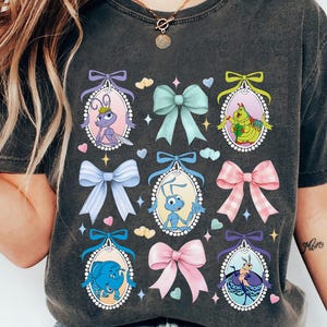 May include: A dark gray t-shirt with a graphic print of cartoon bugs and bows in pastel colors. The bugs are in oval frames with pearl accents. The text "A Bug's Life" is written on the right sleeve.