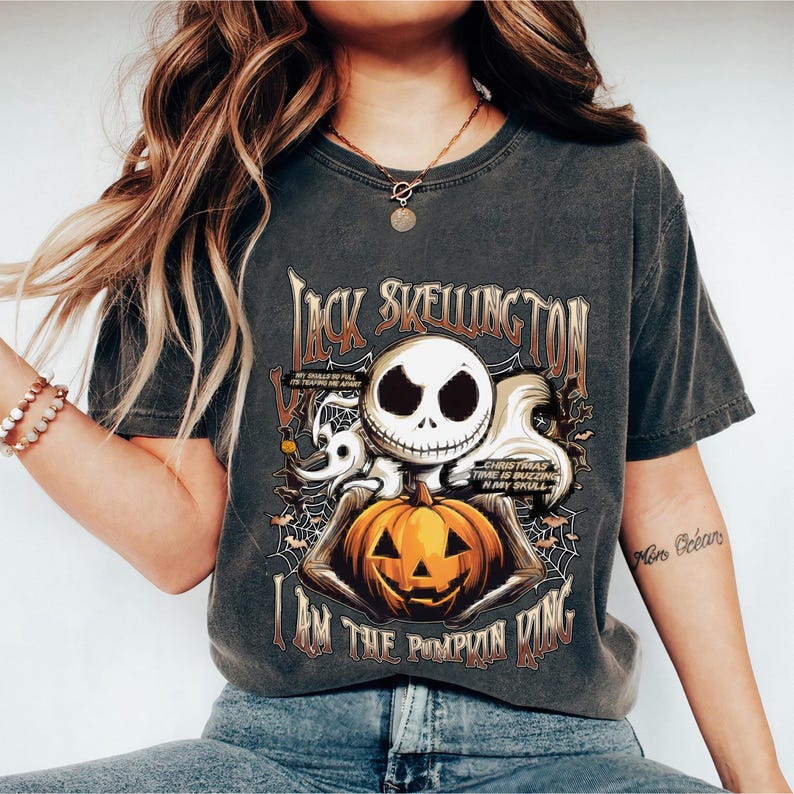 Puede incluir: Camiseta gris oscuro con Jack Skellington sosteniendo una calabaza tallada. La camiseta tiene el texto "Jack Skellington" y "I am the Pumpkin King". El dise&ntilde;o incluye a Zero, telara&ntilde;as y el texto "Christmas time is buzzing in my skull."