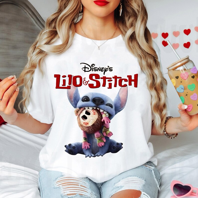 Może przedstawiać: Biała koszulka z logo Disney's Lilo & Stitch w kolorze czerwonym i czarnym. Grafika przedstawia Stitcha, niebieskiego kosmitę, trzymającego brązowego misia. Koszulka ma okrągły dekolt.