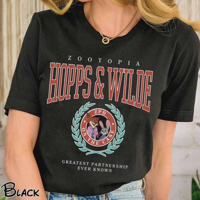 Op de afbeelding: Zwart T-shirt met de tekst "ZOOTOPIA HOPPS & WILDE" in rode en witte letters. Een cirkelvormige afbeelding toont stripfiguren en de woorden "ON THE CASE". De zin "GREATEST PARTNERSHIP EVER KNOWN" staat eronder gedrukt.