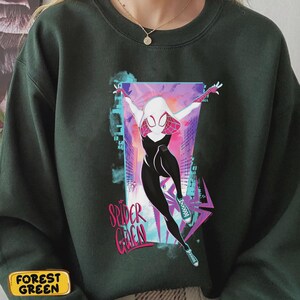 May include: Forest green sweatshirt featuring a graphic of Spider-Gwen in a dynamic pose. The design includes a white and pink mask, black and white suit, and the words "Spider Gwen" in pink. The background has a cityscape design.