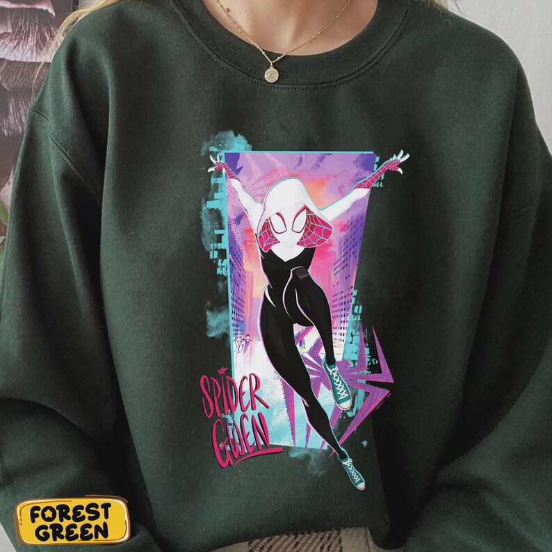 May include: Forest green sweatshirt featuring a graphic of Spider-Gwen in a dynamic pose. The design includes a white and pink mask, black and white suit, and the words "Spider Gwen" in pink. The background has a cityscape design.