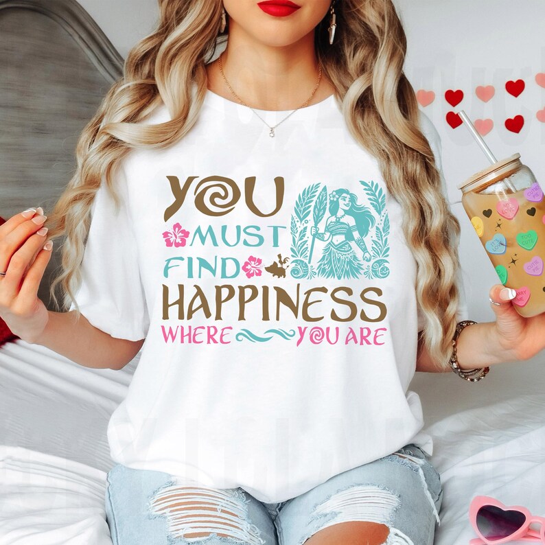 May include: White t-shirt with a brown and blue graphic design featuring a cartoon character and the text "You must find happiness where you are."
