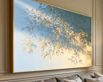 Puede incluir: Una gran pieza de arte mural rectangular que presenta una pintura de enfoque suave de ramas de árboles con hojas de color amarillo dorado sobre un cielo azul pálido, encerrada en un marco dorado fino, montada sobre un sofá gris con cojines.