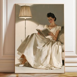 Puede incluir: Una impresión de arte mural enmarcada que representa a una persona de cabello oscuro con un vestido color crema, sentada en un sofá y leyendo un libro abierto. Una lámpara de pie con pantalla plisada a la izquierda ilumina la escena.