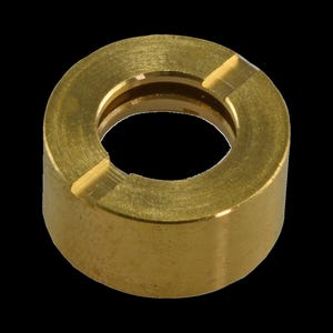 Puede incluir: Primer plano de un anillo de latón con forma cilíndrica. El anillo tiene una abertura circular en el centro y dos ranuras anguladas en el borde superior. El metal tiene un color dorado brillante.