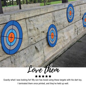 May include: Four blue and grey dart targets with orange and white centres are mounted on a stone wall. The targets are arranged in a row, with the largest target on the left and the smallest target on the right. The targets are made of a durable material and are perfect for use with darts.