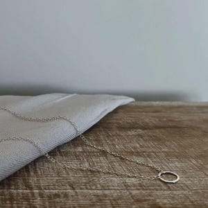 May include: A silver chain necklace with a simple circle pendant. The necklace is lying on a wooden surface.