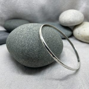 May include: A silver hammered bangle bracelet. The bracelet is smooth and shiny, and it has a simple, elegant design.