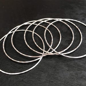 May include: A set of six silver bangles, each with a hammered texture. The bangles are stacked on top of each other, creating a layered effect.