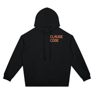 Puede incluir: Una sudadera con capucha negra que presenta un bolsillo tipo canguro frontal y mangas largas. El texto CLAUDE CODE está impreso en la parte superior izquierda del pecho en una fuente naranja pixelada con un efecto de sombra oscura.