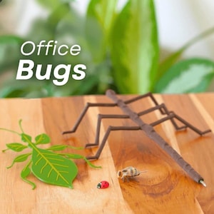 May include: A wooden desk with a variety of insect-themed office supplies. A brown stick insect pen, a green leaf-shaped paper clip, a small ladybug, and a bee-shaped object are arranged on the desk. The words "Office Bugs" are in white text.