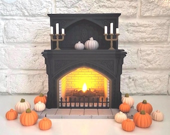 May include: A black miniature fireplace with a lit fire and two gold candle holders. White and orange pumpkins are arranged around the fireplace. The fireplace has a decorative design and is set against a white brick wall.