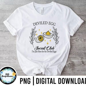 Puede incluir: Camiseta blanca con el texto "DEVILED EGG Social Club" y una ilustración de huevos rellenos. La camiseta también incluye la frase "I'm Just Here for the Deviled Eggs".