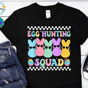Puede incluir: Camiseta negra con un borde a cuadros y el texto "Egg Hunting Squad". Cuatro píos de colores pastel con gafas de sol están dispuestos en fila. Cada pío tiene un patrón a cuadros.