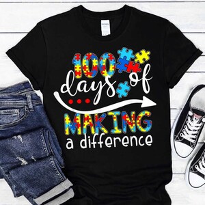 May include: Black t-shirt with a white graphic that says "100 days of making a difference". The graphic includes a puzzle piece design in red, blue, yellow, and green.