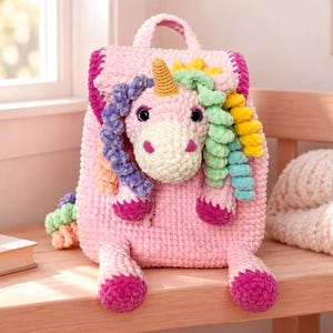 May include: A pink crochet backpack shaped like a unicorn with a cream-coloured muzzle, a yellow horn, and a mane made of curly yarn in shades of purple, green, and yellow. The bag features dark pink accents on the hooves and trim.
