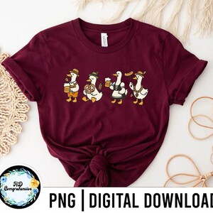 May include: Burgundy t-shirt featuring a whimsical illustration of four ducks in traditional Bavarian attire. Each duck is depicted with a different accessory, including beer steins, pretzels, and sausages. The text "PNG | DIGITAL DOWNLOAD" is at the bottom.