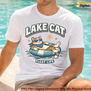 May include: White t-shirt featuring a cartoon cat wearing sunglasses and a bandana, lounging on an inner tube. The shirt has the words "LAKE CAT" above the cat and "FLOAT LIFE" below. A sun graphic is also present.