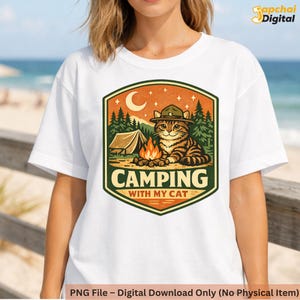 May include: White t-shirt featuring a camping-themed graphic. The design includes a cat wearing a ranger hat, a campfire, a tent, and the text "CAMPING WITH MY CAT". The graphic is set against a backdrop of trees and a crescent moon.